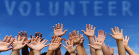 Many hands up in the air with blue sky background and volunteer above in sky writing