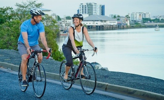 Two bicycle riders looking at each other riding on the river front.