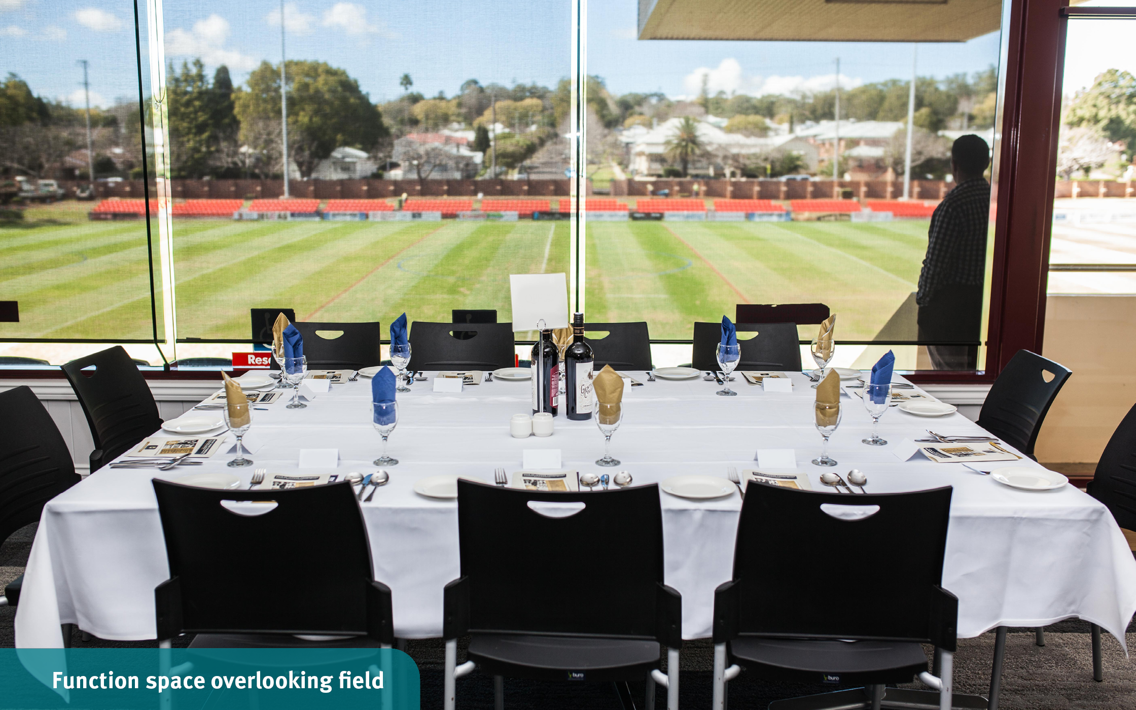 Elegant dining table set with dinnerware and wine glasses overlooking the green outdoor field from the function room at the Toowoomba Sports Grounds.