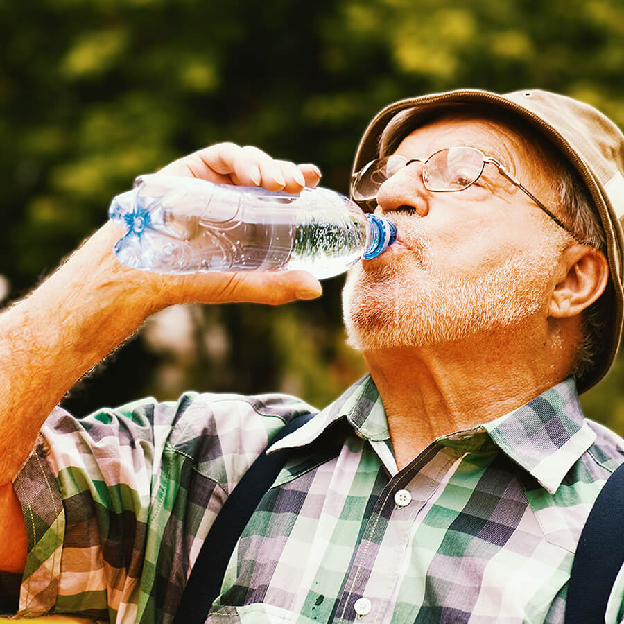 An elderly man drinks water on a hot day.