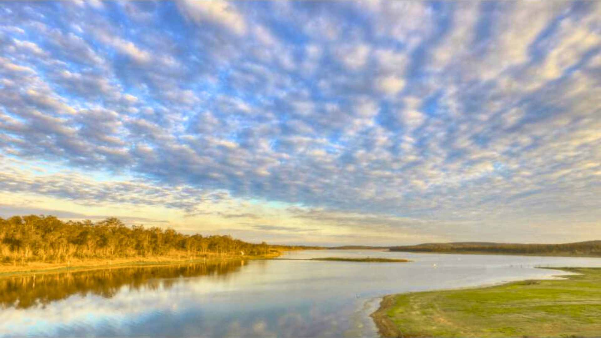 Wide reservoir with open water, grassy shoreline and a cloudy sky.
