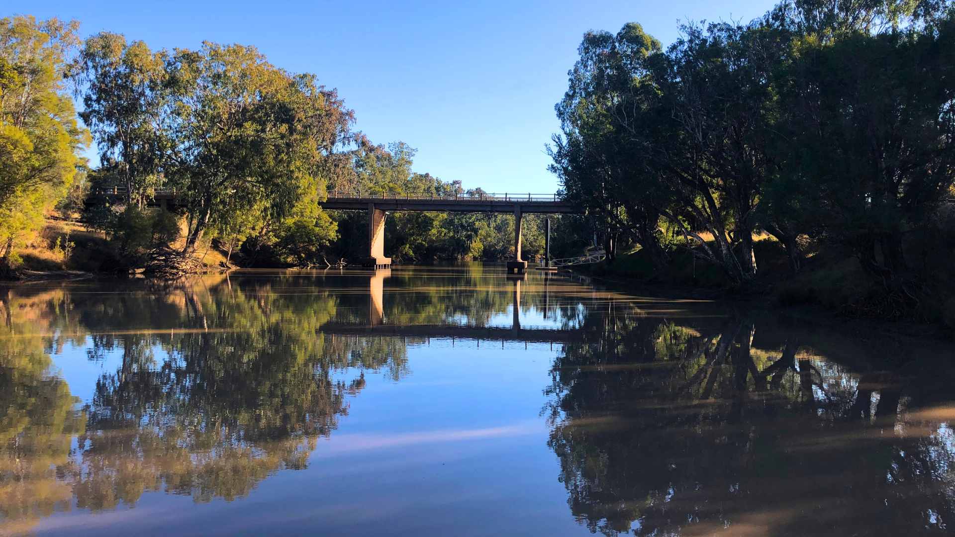 River pool at Surat Weir with reflections of trees and bridge crossing.