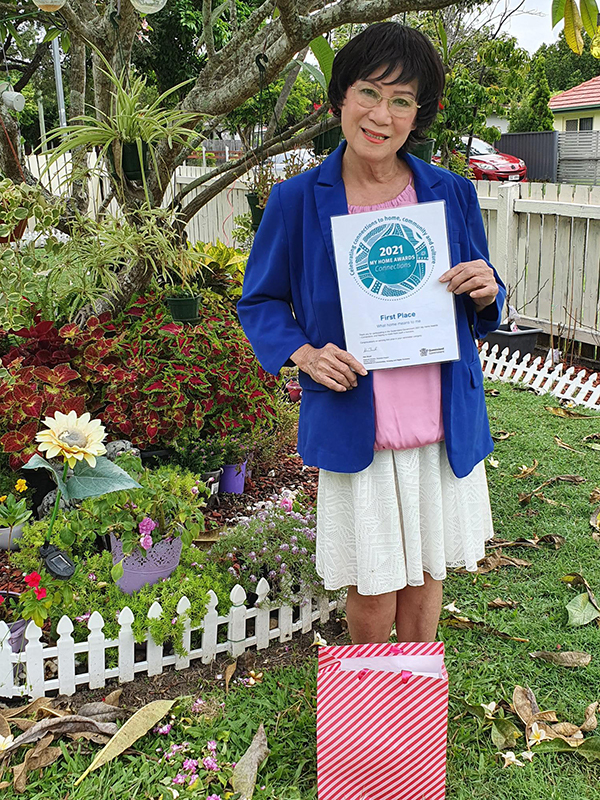 Giao holds her award certificate while standing in front of one of her beautiful garden beds.