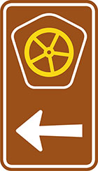 brown sign with pentagonal badge with yellow steering wheel, as well as an arrow