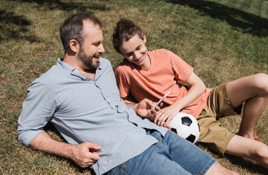 older male and younger male laying on the grass chatting with a soccer ball 