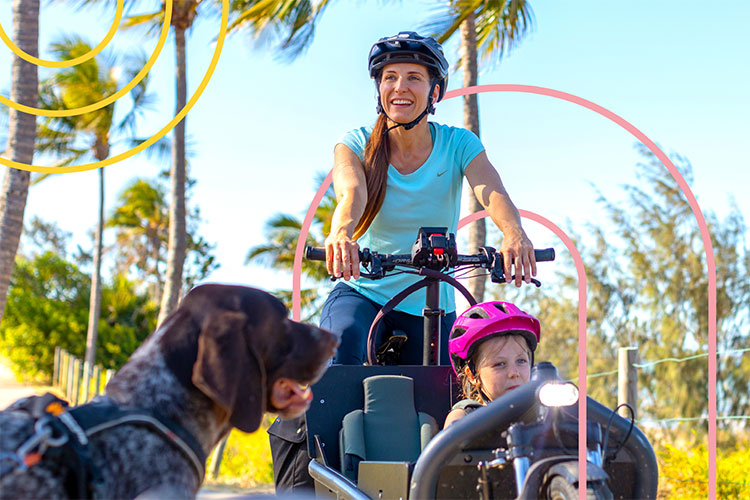 Woman wearing a helmet while riding a bike with a child carrier in front. 