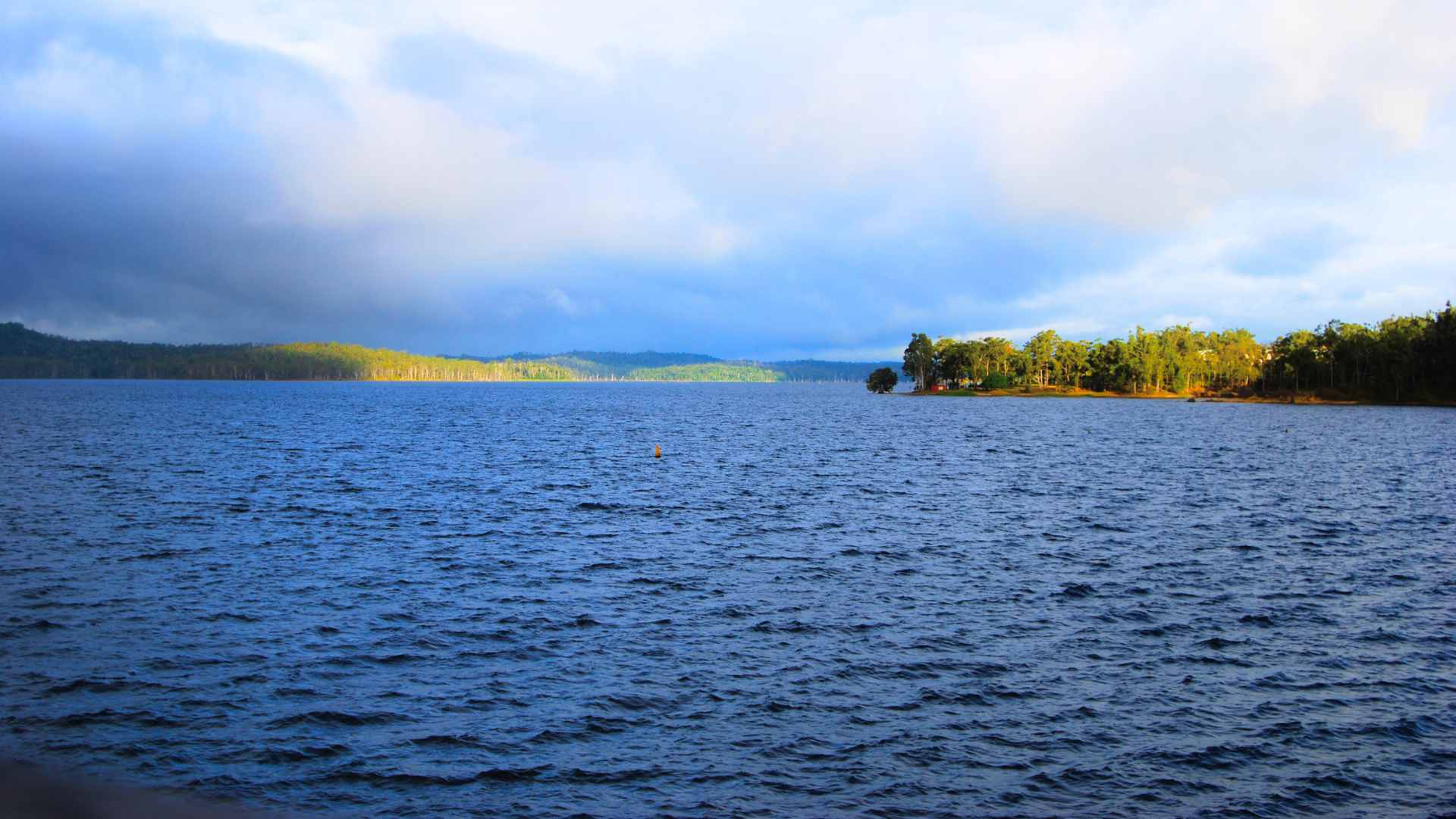 Wide reservoir with deep blue water, forested hills and distant shoreline.