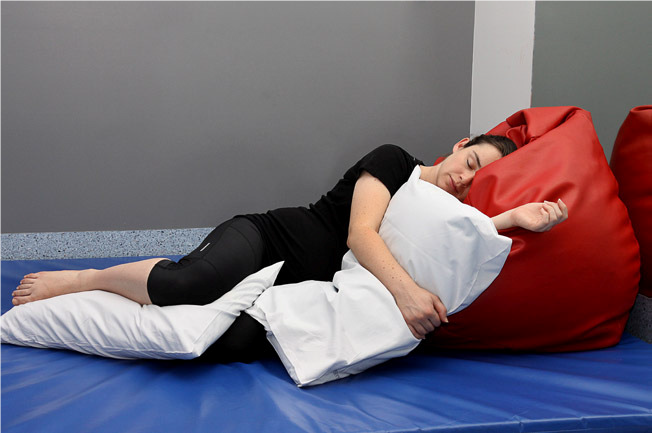 Pregnant woman lying on her left side, head and shoulders on a bean bag with pillows between her knees and arms.
