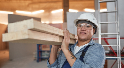 Young woman in hard hat on building site carrying wood.