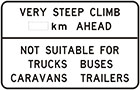 white sign with black text, very steep climb number of km ahead. Not suitable for trucks buses caravans trailers