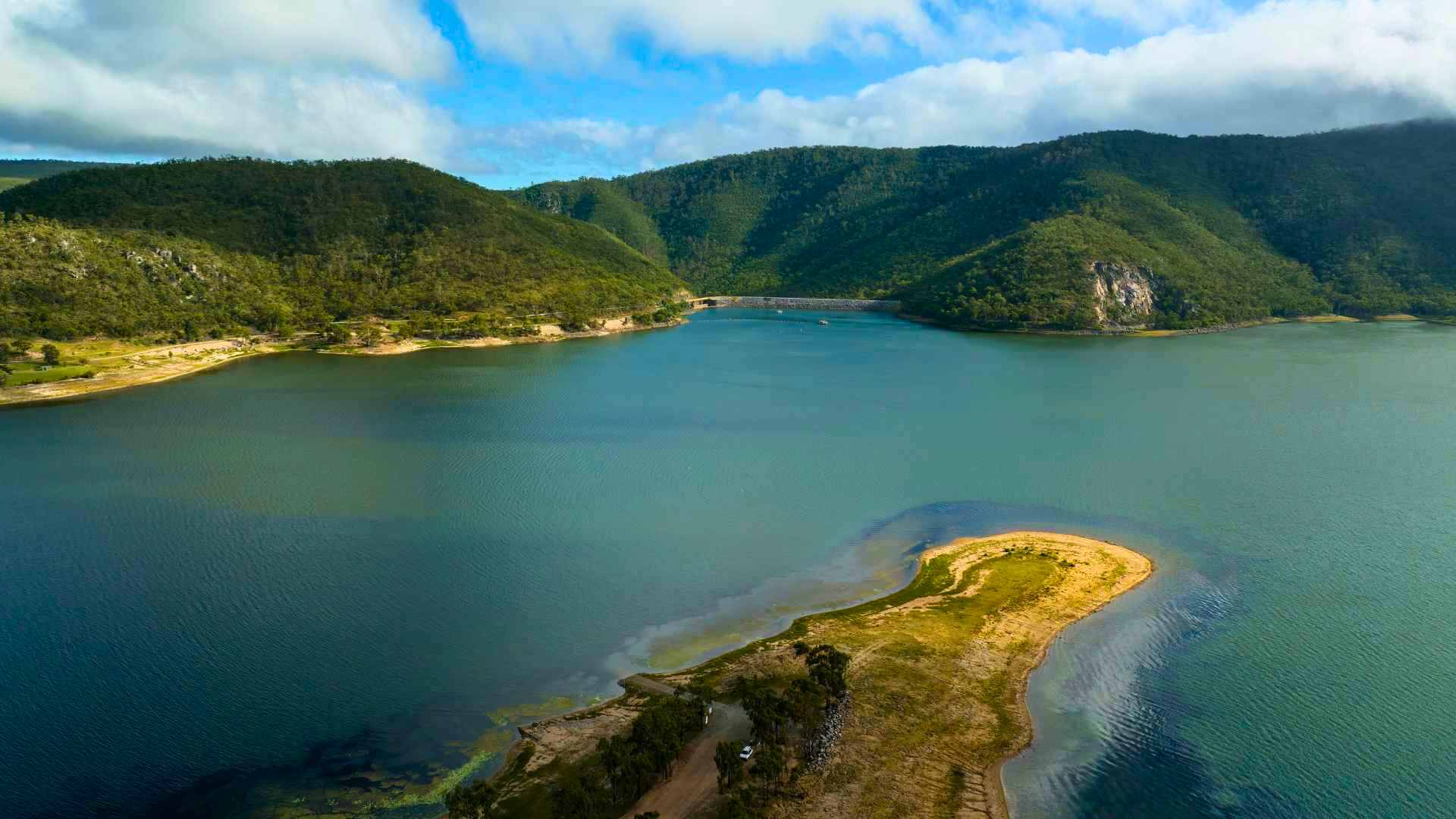 Large open dam with surrounding hills and grassy shoreline.