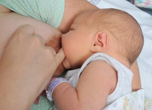 Baby breastfeeding, mother has her little finger in the corner of the baby’s mouth.