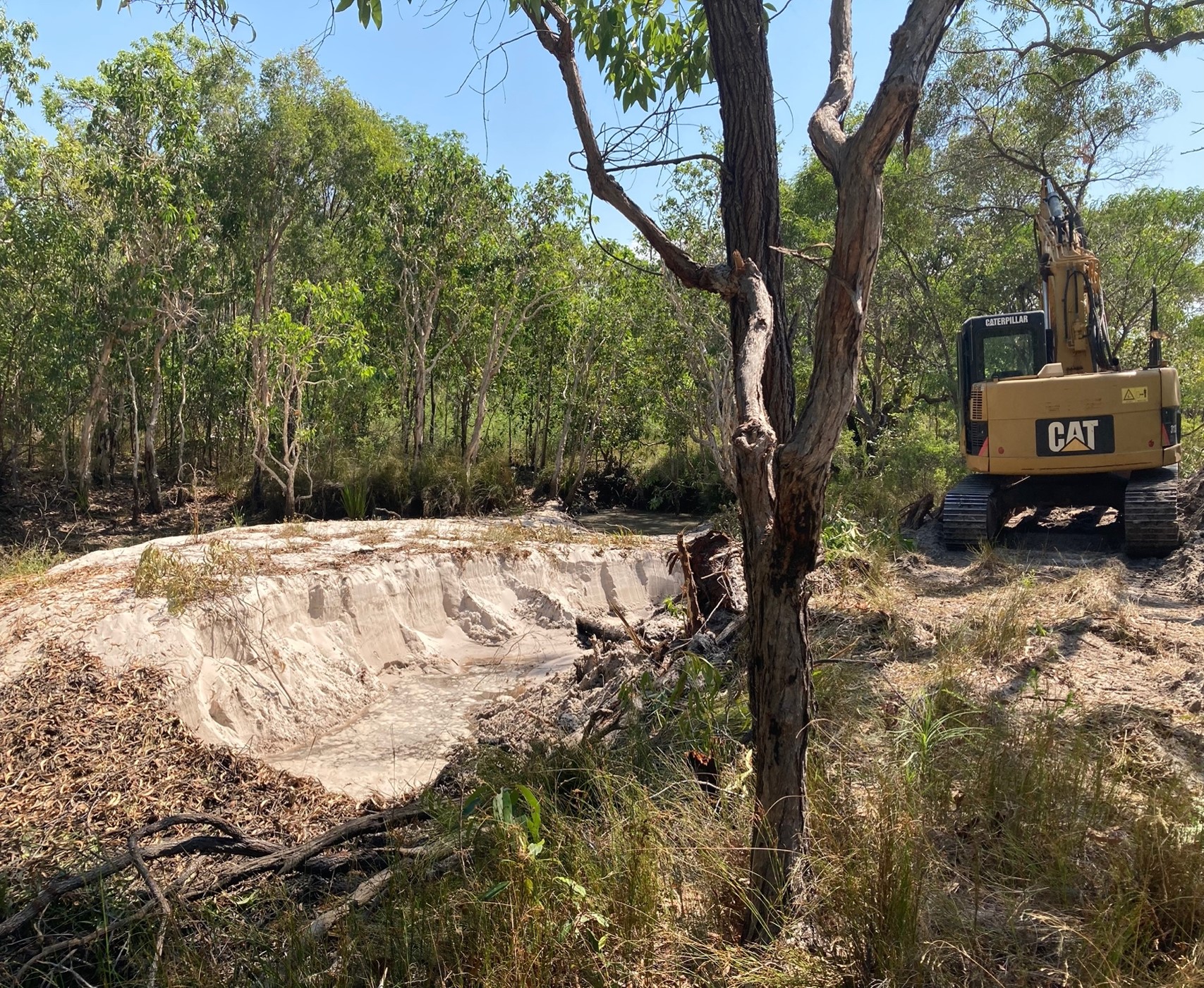 Bank of sandy sediment piled up in a lagoon with excavator in background.