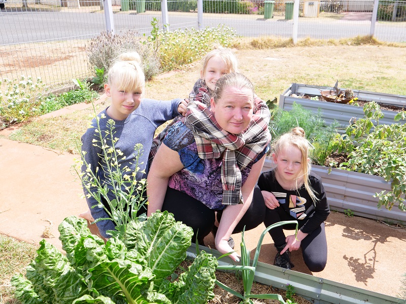 Ella with her mum Sarah, and her sisters kneeling by their vegie patch.