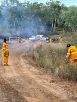 Rangers in high visibility jackets monitoring small cool fire along roadside