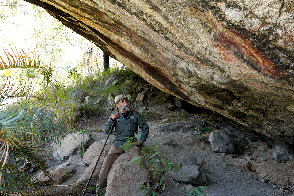 Buluwai Elder and Cultural Custodian sitting on a rock under a tree