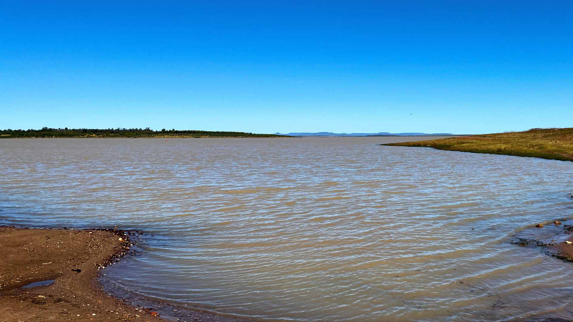 Expansive reservoir stretching to the horizon with low grassy banks.