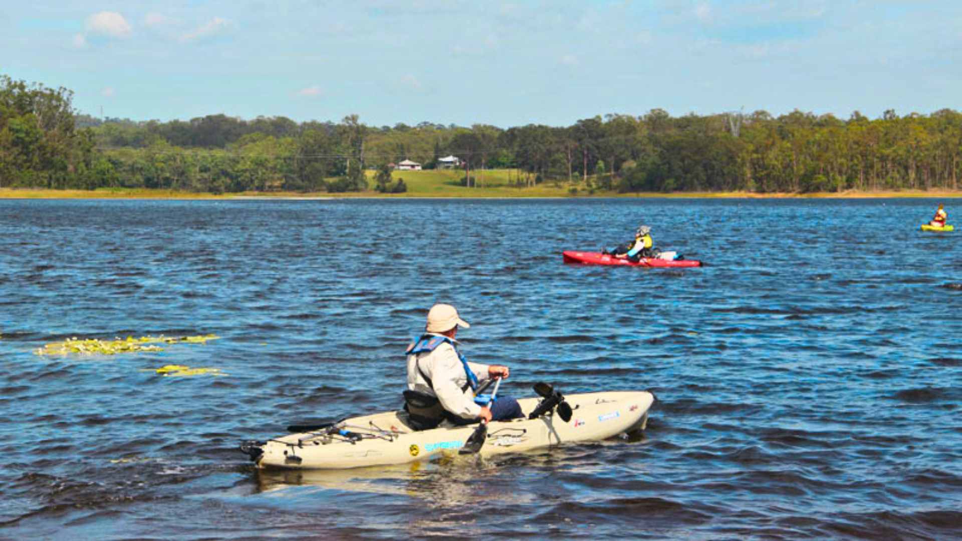 Kayakers paddling across Lake Kurwongbah with forested banks.