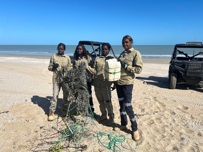 Four students on beach holding discarded fishing net. 
