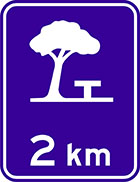 blue sign with white icon of a picnic table under a tree and the text 2km