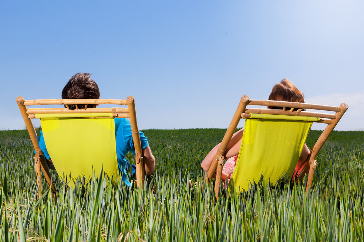 Two people sitting in deck chairs in long green grass looking up at a clear blue sky