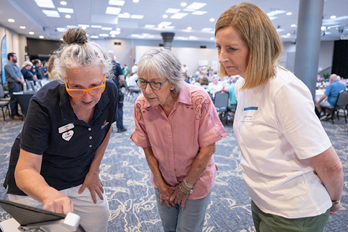 Three women, two are showing a Seniors Expo participant something on a tablet.