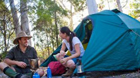 Two campers outside their tent with a small gas stove.