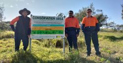 Photo of 3 rangers standing next to a sign about a beach restoration project.