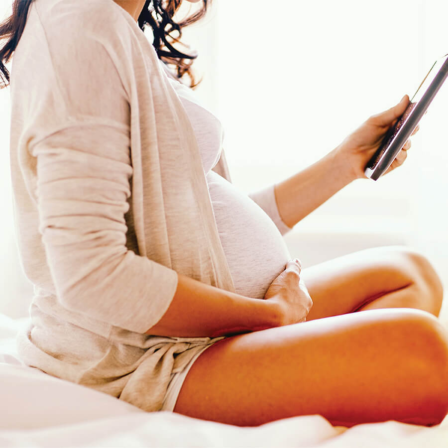 A pregnant woman reads from a tablet.