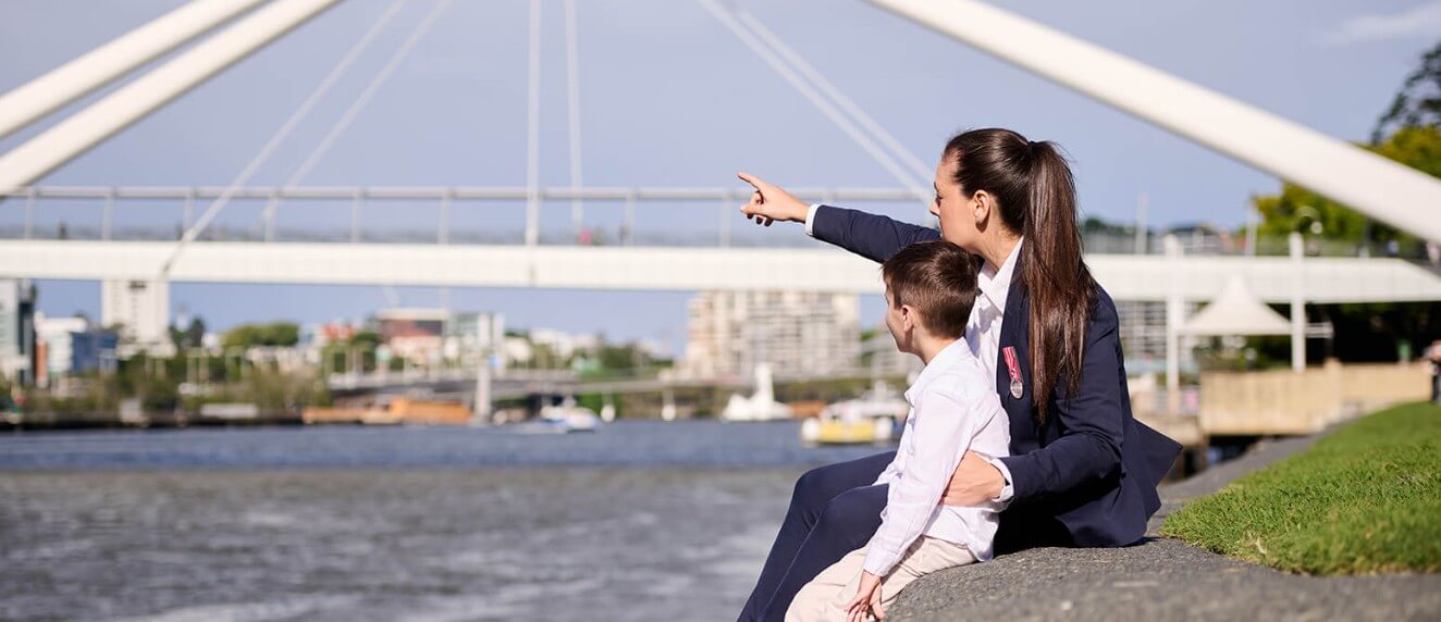 A woman and child sit on a rock by a river, enjoying nature and each other's company.