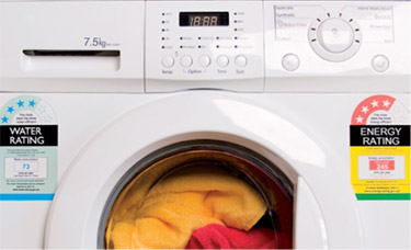 Front load washing machine with water and energy efficiency rating stickers. There are red and yellow garments in he machine.