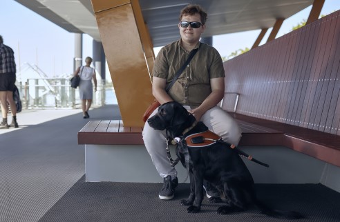 A young man is seated with his guide dog