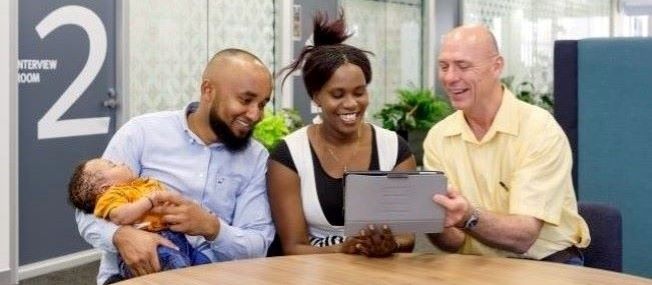 Young family with consultant around a table outdoors looking at a tablet.